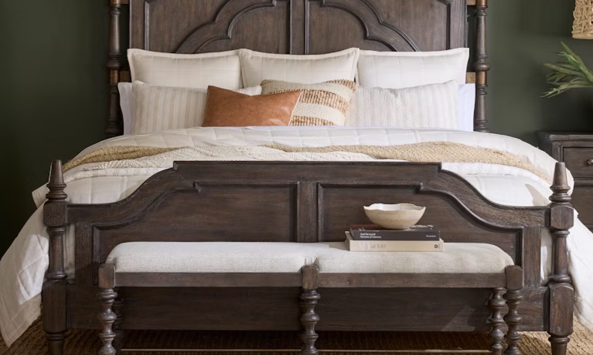 Rustic dark wood panel bed with intricately carved headboard, styled with neutral bedding, a textured rug, and a cozy bench at the foot.
